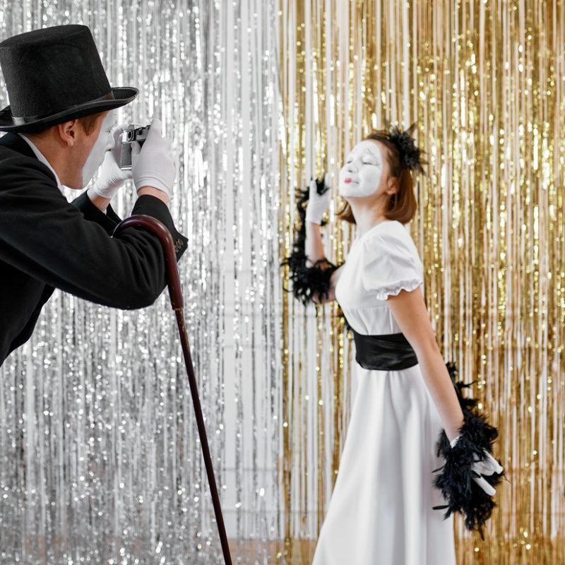 Two mime artists, lady poses at gentleman with camera. Pantomime theater, parody comedian, positive emotion, humour performance, funny face mimic and grimace