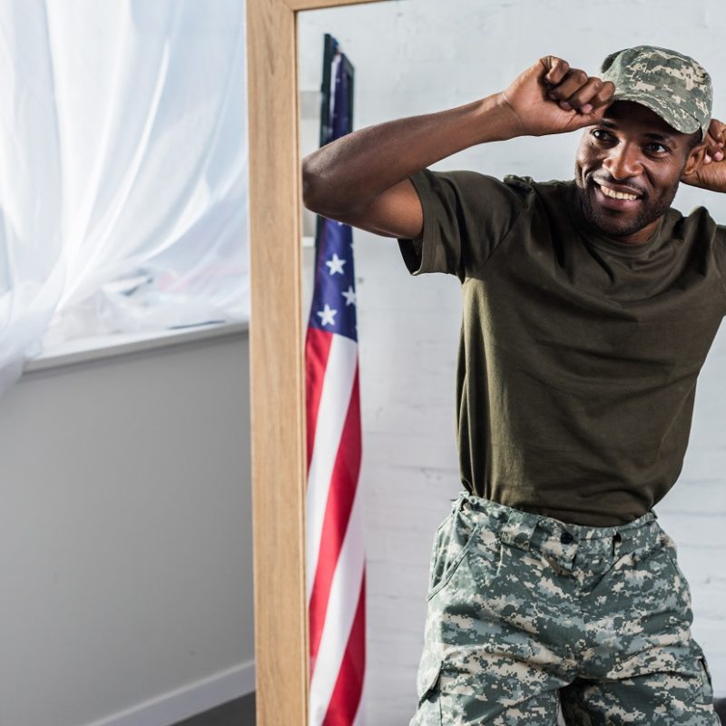 Smiling african american soldier in camouflage clothes posing by the mirror